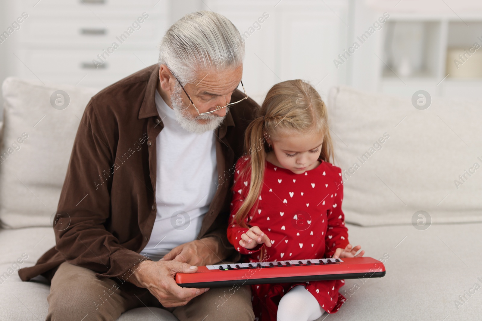 Photo of Grandpa and his granddaughter playing toy piano on sofa at home