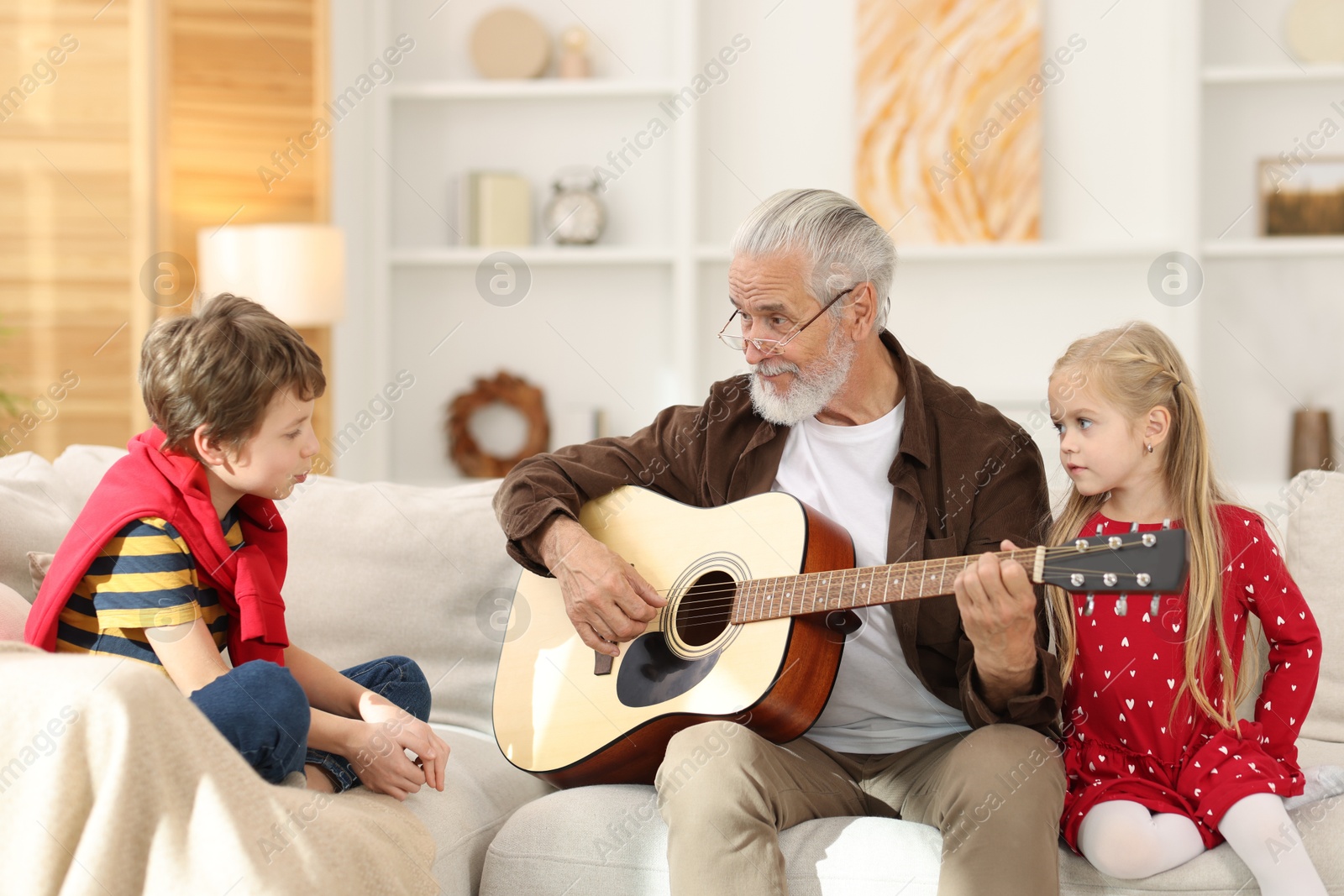 Photo of Grandpa playing guitar for his grandkids on sofa at home