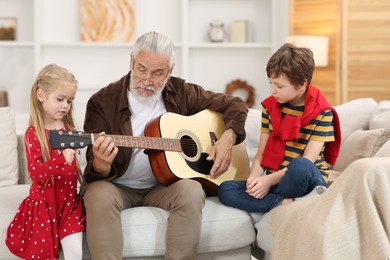 Grandpa playing guitar for his grandkids on sofa at home