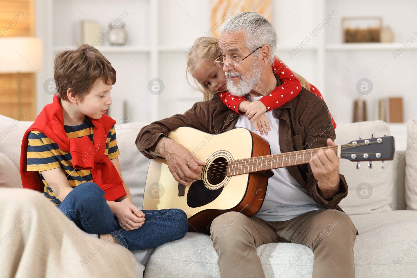 Photo of Grandpa playing guitar for his grandkids on sofa at home