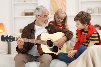 Photo of Grandpa playing guitar for his grandkids on sofa at home