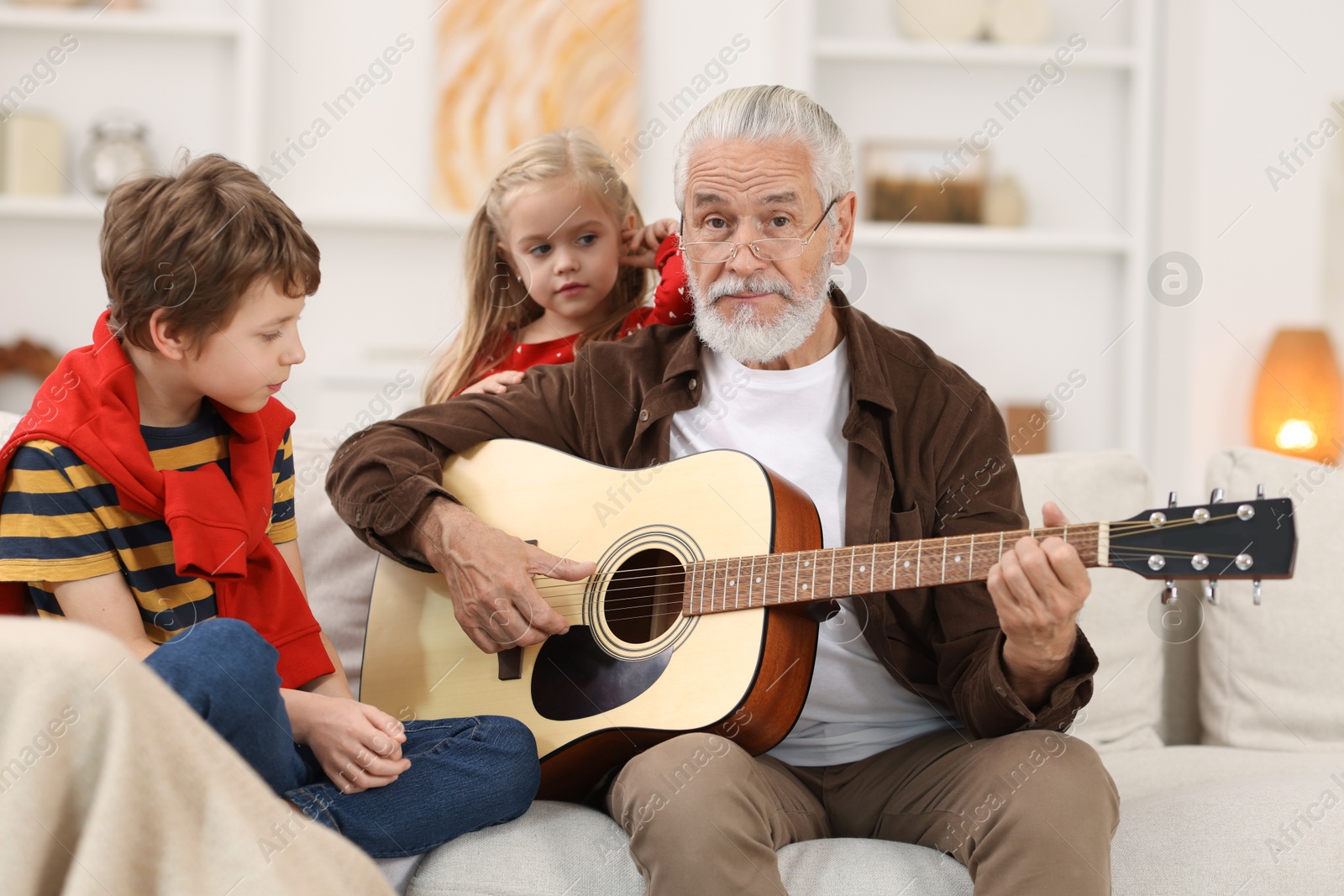 Photo of Grandpa playing guitar for his grandkids on sofa at home