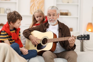 Photo of Grandpa playing guitar for his grandkids on sofa at home