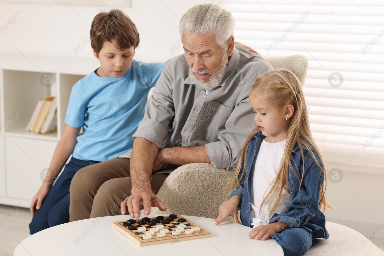 Photo of Grandpa and his grandkids playing checkers at table indoors