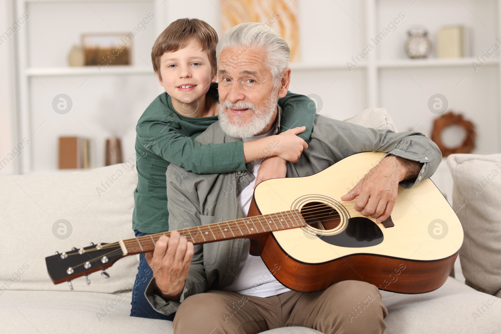 Photo of Grandpa teaching his grandson to play guitar on sofa at home