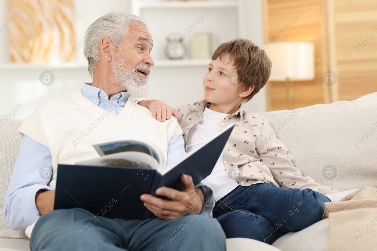 Photo of Grandpa and his grandson reading book together on sofa at home