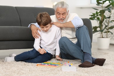 Grandpa and his grandson playing with math game Times table tray on floor at home