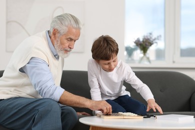 Grandpa and his grandson playing checkers at table indoors