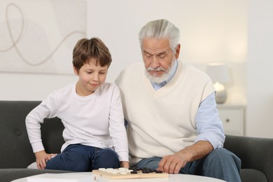 Photo of Grandpa and his grandson playing checkers at table indoors