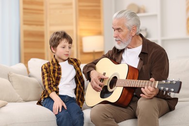 Grandpa teaching his grandson to play guitar on sofa at home