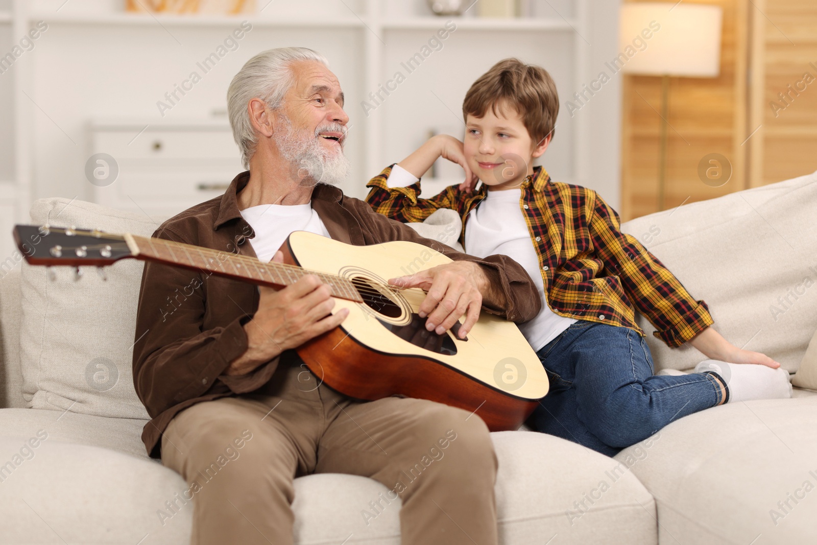 Photo of Grandpa teaching his grandson to play guitar on sofa at home