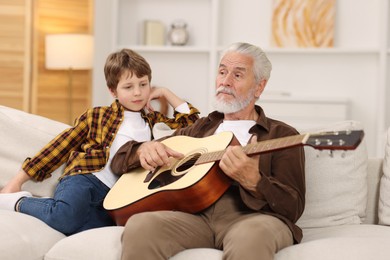 Photo of Grandpa teaching his grandson to play guitar on sofa at home