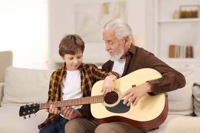 Photo of Grandpa teaching his grandson to play guitar on sofa at home