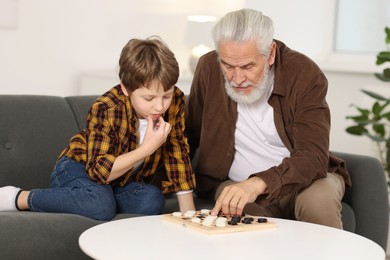 Grandpa and his grandson playing checkers at table indoors