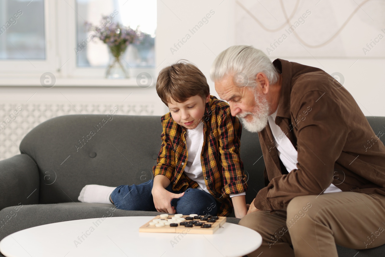 Photo of Grandpa and his grandson playing checkers at table indoors