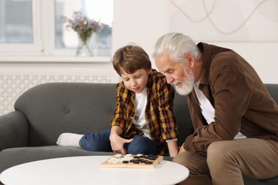 Grandpa and his grandson playing checkers at table indoors