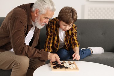 Photo of Grandpa and his grandson playing checkers at table indoors