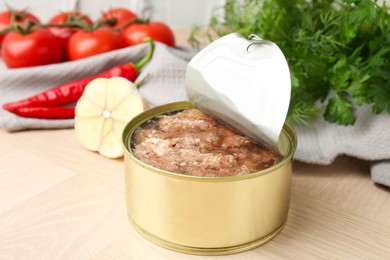 Photo of Canned meat in tin can and other products on wooden table, closeup