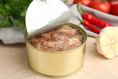 Photo of Canned meat in tin can and other products on wooden table, closeup