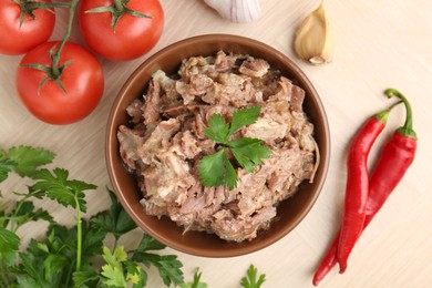 Photo of Canned meat in bowl, parsley, tomatoes, garlic and chili peppers on wooden table, top view