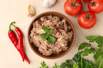 Photo of Canned meat in bowl, parsley, tomatoes, garlic and chili peppers on wooden table, top view