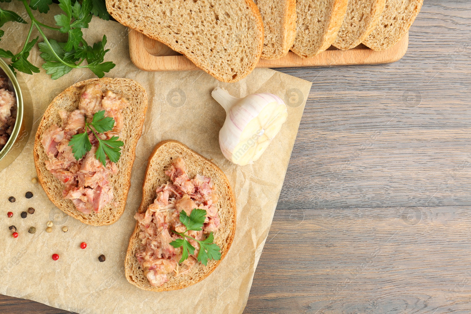 Photo of Sandwiches with canned meat, parsley, garlic and peppercorns on wooden table, top view. Space for text