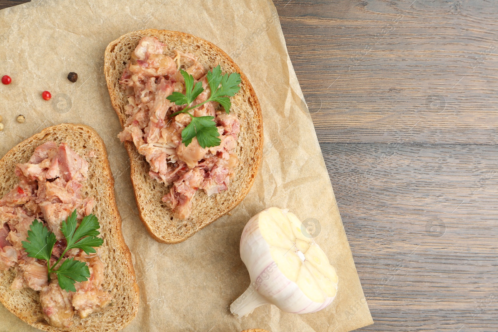 Photo of Sandwiches with canned meat, parsley, garlic and peppercorns on wooden table, top view. Space for text