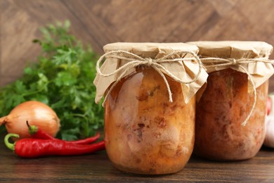 Photo of Canned meat in glass jars, chili peppers, onion and parsley on wooden table