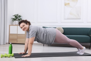 Photo of Woman doing plank exercise on fitness mat at home