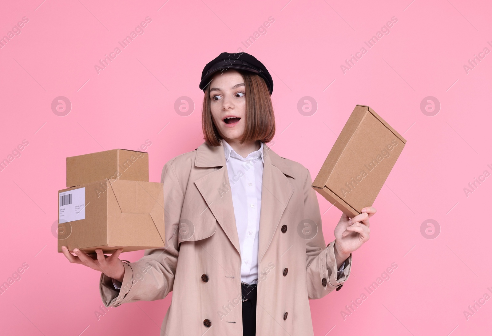 Photo of Surprised postwoman with parcels on pink background