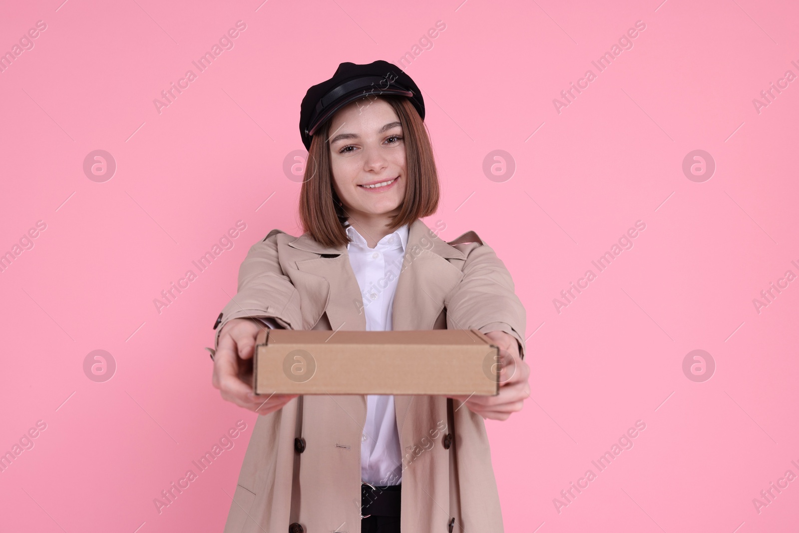 Photo of Happy postwoman giving parcel on pink background