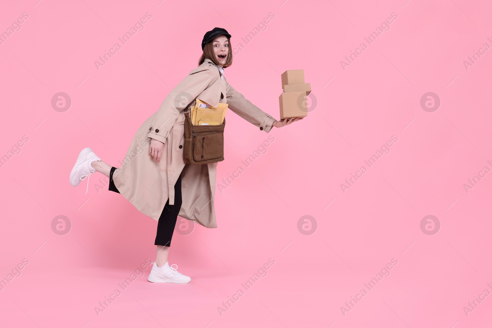 Photo of Happy postwoman with bag and parcels on pink background. Space for text