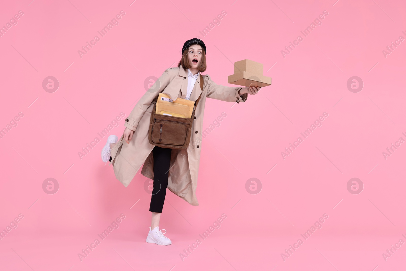 Photo of Emotional postwoman with bag and parcels on pink background. Space for text