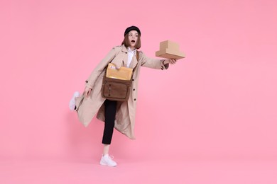 Photo of Emotional postwoman with bag and parcels on pink background. Space for text