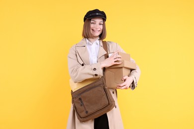 Photo of Happy postwoman with bag and parcels on yellow background