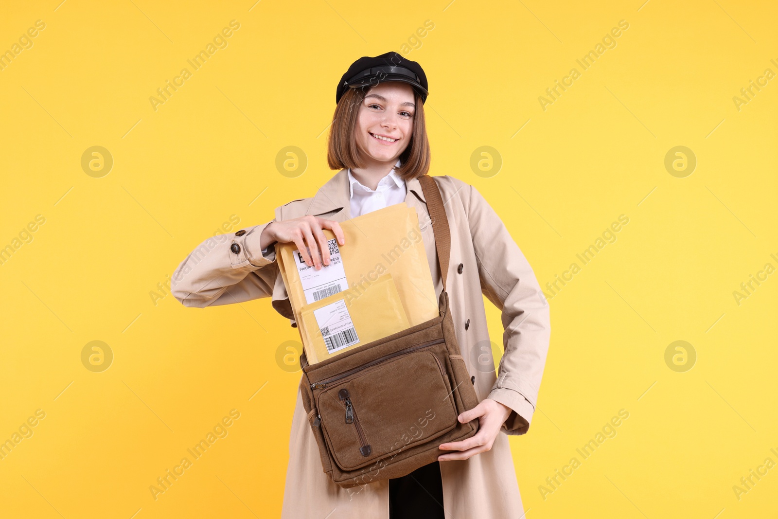 Photo of Happy postwoman with bag and envelopes on yellow background