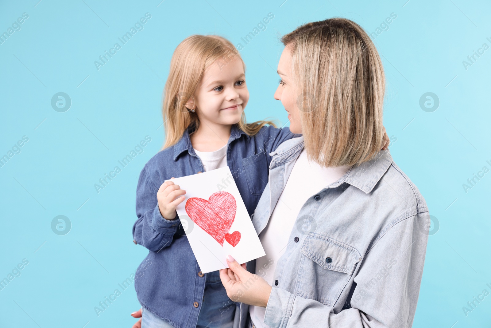 Photo of Little daughter congratulating her mom with greeting card on light blue background. Happy Mother's Day