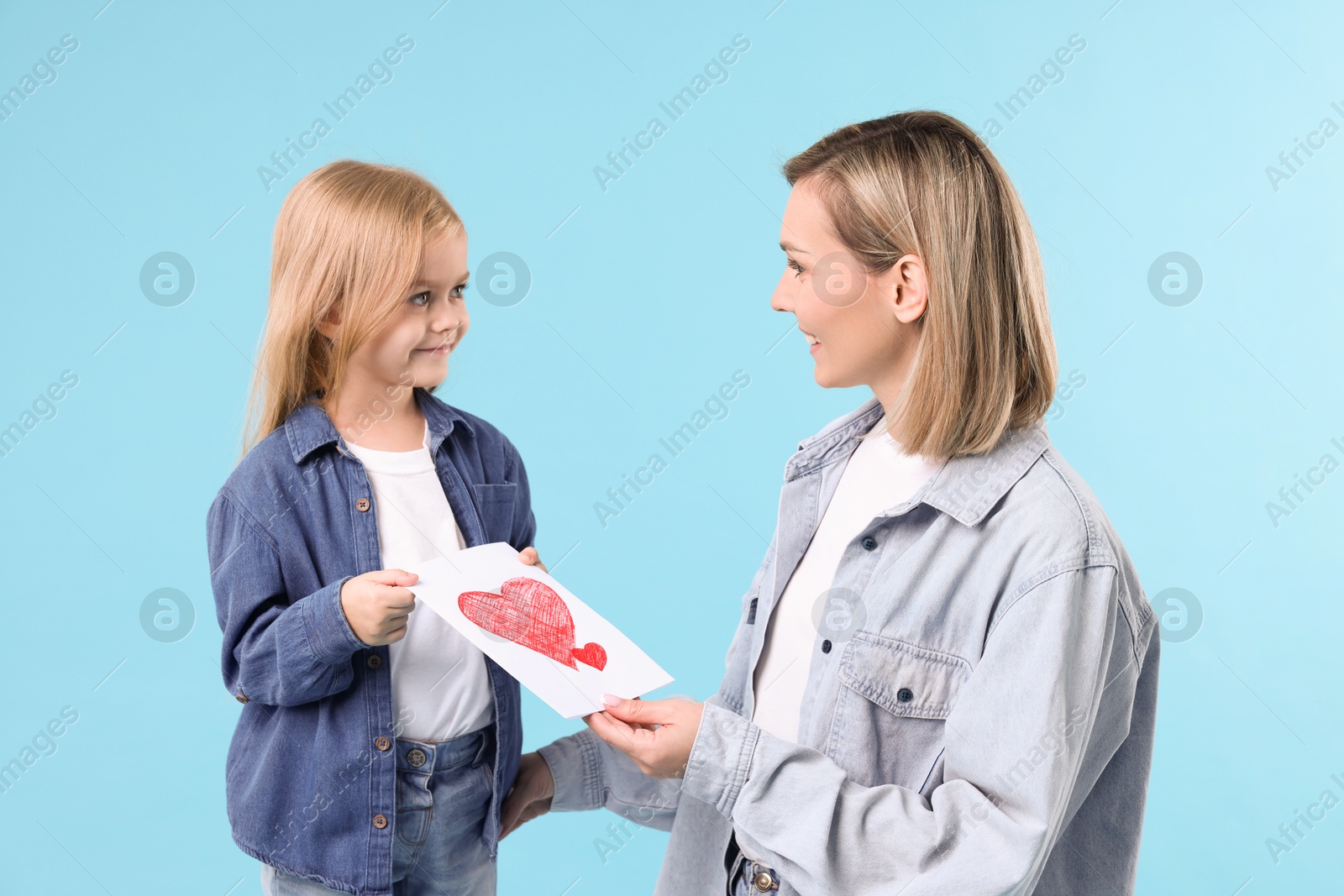 Photo of Little daughter congratulating her mom with greeting card on light blue background. Happy Mother's Day