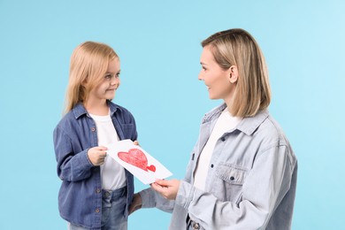 Little daughter congratulating her mom with greeting card on light blue background. Happy Mother's Day