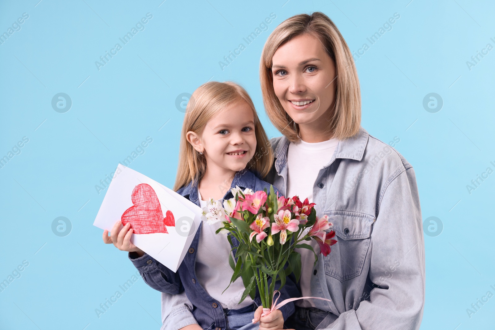 Photo of Little daughter congratulating her mom with bouquet of alstroemeria flowers and greeting card on light blue background. Happy Mother's Day