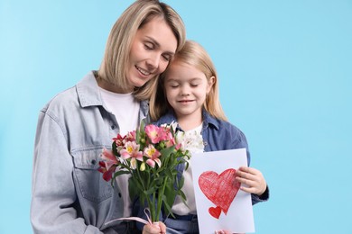 Photo of Little daughter congratulating her mom with bouquet of alstroemeria flowers and greeting card on light blue background, space for text. Happy Mother's Day