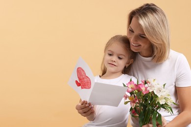 Photo of Happy woman with her daughter, bouquet of alstroemeria flowers and greeting card on beige background, space for text. Mother's Day celebration