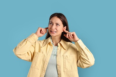 Photo of Annoyed woman covering her ears due to loud sound on light blue background