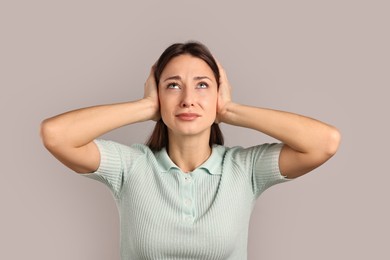 Annoyed woman covering her ears due to loud sound on light grey background