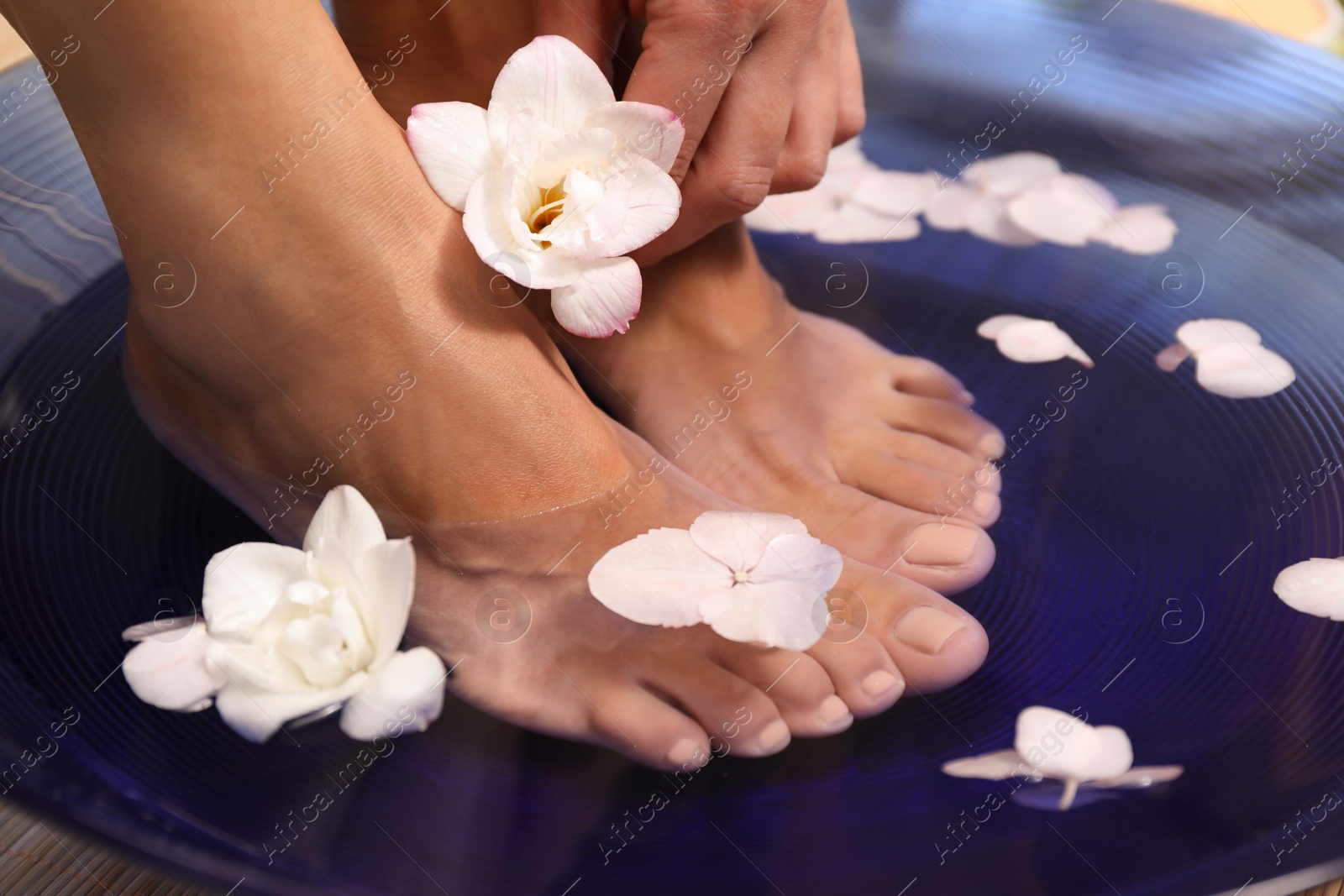 Photo of Woman soaking her feet in bowl with water and flowers, closeup. Spa treatment