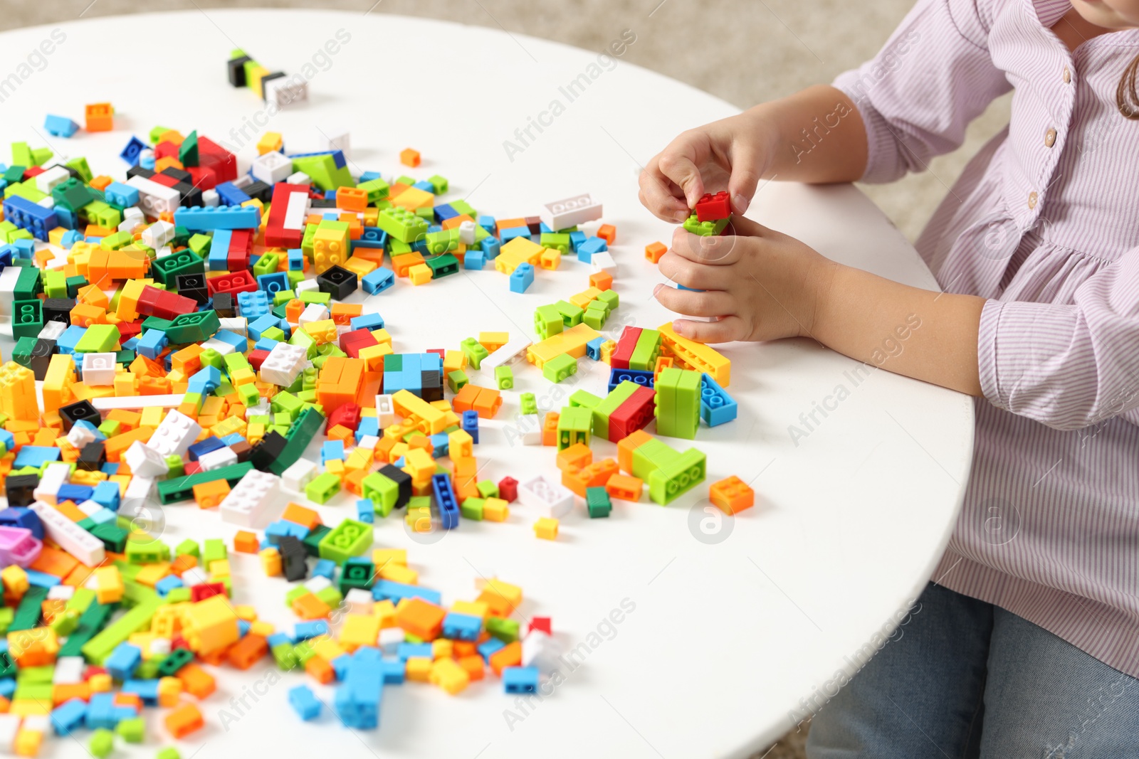 Photo of Girl playing with building blocks at white table indoors, closeup