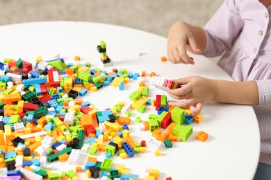 Photo of Girl playing with building blocks at white table indoors, closeup