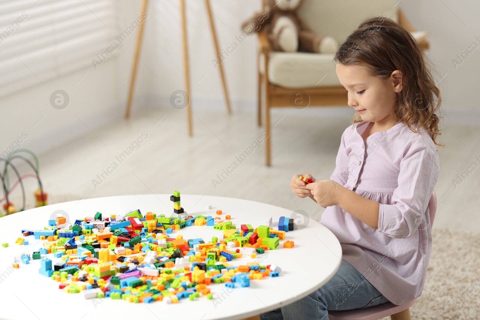 Photo of Cute girl playing with building blocks at white table indoors