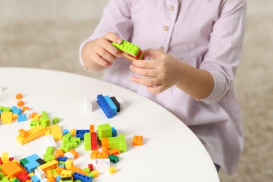 Photo of Girl playing with building blocks at white table indoors, closeup