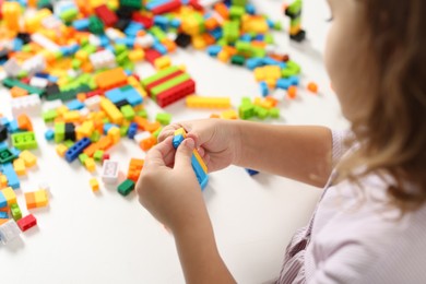 Photo of Girl playing with building blocks at white table indoors, closeup